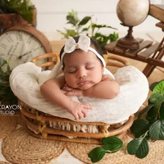 This setup features a sleeping newborn in a basket surrounded by vintage-inspired props like a clock and globe, suggesting the timeless journey of life ahead.