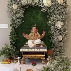 A premium backdrop for a Ganapathi festival. The idol is placed within a beautiful arch of baby's breath and white roses against a green wall, creating a fresh and elegant look.