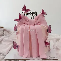 A pretty pink cake featuring a large, beautifully crafted pink bow and delicate butterflies. It's a very trendy and feminine design, perfect for a stylish birthday.