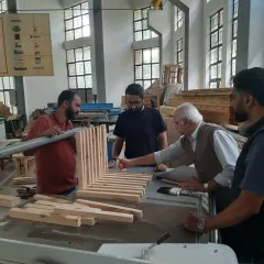 Teamwork in the workshop. Students collaborate on a project at the table saw under the watchful eye of their trainer, learning how to manage larger pieces of material.