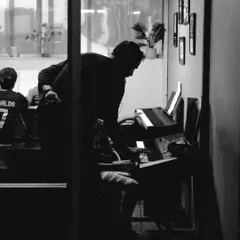 A teacher provides individual guidance during a piano lesson. This black and white shot captures a quiet moment of focused learning.