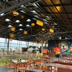 This shot of The Soda Factory showcases the full ambiance at dusk. The strategic placement of plants around the seating areas and the vibrant wall mural come together to create an energetic and inviting atmosphere for guests.