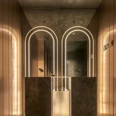 We believe every part of a home deserves great design. This wash area features custom arched backlit mirrors and warm, vertical wall paneling, turning a simple utility space into a statement of modern elegance.