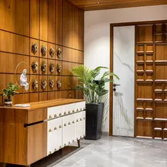 This elegant foyer features a stunning carved wooden door and a console with intricate white detailing. The wall is adorned with decorative brass masks, creating a culturally rich entrance.