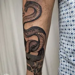 A realistic snake tattoo wrapping around the forearm. The detailed scales and shading, combined with the solid black bands, create a dynamic and powerful design that moves with the arm.