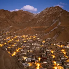 The town of Leh in Ladakh, nestled in a valley and illuminated at dusk. This aerial photograph shows how human settlement coexists with the immense scale of the mountains.