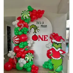 A fun and unique Christmas party theme: "He's a Mean ONE." This Grinch-themed first birthday backdrop includes a character cutout and a balloon garland in the Grinch's signature red, green, and white colors.