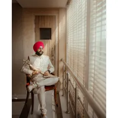 A classic portrait of the groom, Avikash, seated by a window, holding his kirpan. The natural light creates a thoughtful and regal mood.