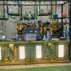 A straight-on view of the elegant gold and green coffee bar. The open shelving provides space for displaying different coffee beans, syrups, and other supplies, adding to the authentic café aesthetic.