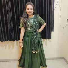 A full-length view of a custom-designed dark green lehenga choli. The combination of the patterned blouse and the simple, flowing skirt with a thick golden border is a classic choice for any festival.