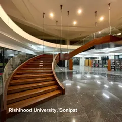 The grand, curving staircase at Rishihood University, Sonipat, serves as a central architectural feature. It connects floors within a large, open-plan space, encouraging movement and visual connection across different levels of the institution.