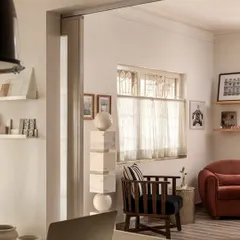 A view from one workspace into a cozy seating area, showing how we create distinct yet connected zones. The mix of a plush sofa, a classic wooden armchair, and sheer curtains creates a soft, inviting atmosphere for informal meetings or quiet reflection.