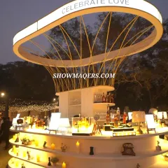 Our custom bar designs are always a centerpiece of the celebration. This stunning, modern circular bar, created for a Roka ceremony, features a unique overhead structure and ambient lighting with the message 'Celebrate Love', making it a focal point for guests to gather and enjoy.