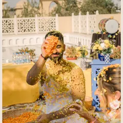 A playful moment during the Haldi ceremony, where the groom is covered in turmeric paste and flower petals, captured in a fun, candid shot.