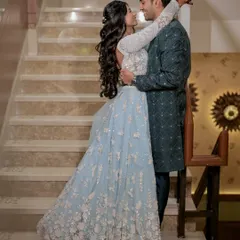 An elegant, full-length portrait that showcases how we guide couples into poses that feel natural and romantic. The soft lighting on the staircase highlights the intricate details of the bride's powder blue lehenga and the groom's coordinating sherwani.
