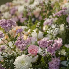 A dreamy close-up of a floral arrangement from a Jaipur wedding. The soft focus highlights a delicate pink rose nestled among a bed of white and lavender chrysanthemums.