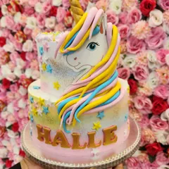 A dreamy two-tiered unicorn cake with a pastel rainbow airbrushed effect. The hand-sculpted fondant unicorn and golden name make it a personalized fantasy creation.