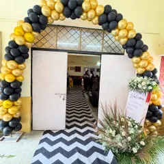 The entrance decoration for a retirement party, featuring a black and gold balloon arch, a welcome sign, and a chevron-patterned carpet runner.