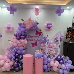 This is a full view of a butterfly-themed decoration I did for a third birthday. It features a large balloon arch in purple and pink, a custom backdrop, large butterfly wings, and matching cake stands.