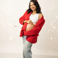 A happy and bright solo portrait from a Christmas session. The mother-to-be wears reindeer antlers and a festive red jacket, glowing with holiday spirit.
