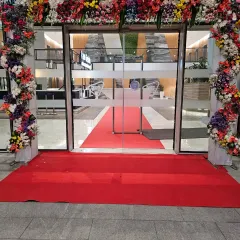 A closer look at a floral entrance arch and red carpet combination for a corporate inauguration. The dense, multi-colored flowers create a vibrant and celebratory first impression for all attendees.