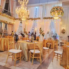 An elegant indoor hall setup for a reception dinner, showing the guest tables with golden tablecloths and the grand chandeliers I installed.