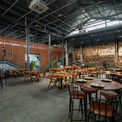 This wide-angle view showcases the scale of the double-volume dining space and two of our signature elements. The rustic terracotta partition wall adds warmth and texture while screening private areas, contrasting beautifully with the industrial metal and concrete surfaces of this modern pub interior.