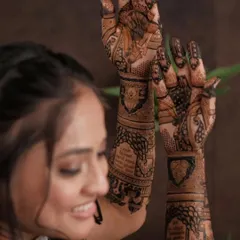 A bride admiring her full-arm mehandi. The design features traditional wedding scenes and intricate patterns, creating a stunning piece of art.