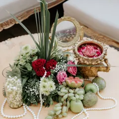 This traditional centerpiece combines fresh flowers, fruits, and pearls with a vintage-style brass mirror, creating a look of classic elegance.