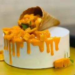 A beautiful Fresh Mango Cake with a gravity-defying cone spilling out fresh mango pieces. This is one of our most popular seasonal cakes, celebrating the king of fruits.