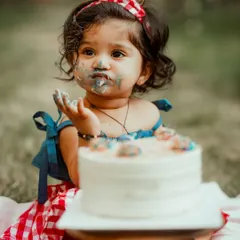 The pure, messy joy of a first birthday cake smash. This close-up shot captures the delightful details, from the frosting on her face to the wonder in her eyes.