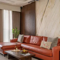 The living room features a bold orange leather sofa that infuses the space with energy. This is balanced by a sophisticated backdrop of book-matched marble and rich wood paneling, creating a dynamic mix of textures.