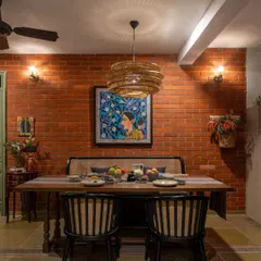 In this Dhaka home, the dining area is set against a warm, exposed brick wall. A large painting adds a vibrant splash of color, while the wicker pendant light brings a touch of natural texture. It’s a space designed for enjoying meals with family and friends.