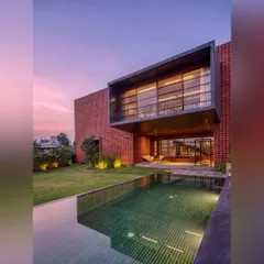 As dusk settles, the homes we design take on a new life. Here, the warm glow from the interior reflects on the pool, while the landscape lighting begins to highlight the textures of the brick facade and the surrounding greenery, creating a tranquil evening ambiance.