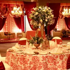 An elegant table setting for the "Noor-e-Kashmir" event, featuring custom printed tablecloths and tall floral centerpieces, all within a space draped in rich red fabrics.