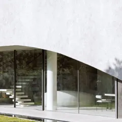 The minimalist glass facade of Villa KD 45, which allows for uninterrupted views of the garden. The floating staircase inside is visible, adding a touch of sculptural elegance to the interior.