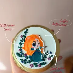 Your favorite characters can become edible art. Here, I hand-drew Merida from 'Brave' using colored buttercream, adding delicate buttercream leaves and flowers to frame the design on this coffee-flavored bento cake.
