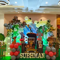 A Lion King inspired jungle theme with a detailed backdrop of Pride Rock. The scene is framed by a balloon arch and includes character cutouts of Simba, Timon, and Pumbaa.