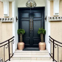 A grand entrance sets the tone for the entire home. Here, two braided Ficus trees in elegant copper-toned planters flank the main door, creating a symmetrical and sophisticated welcome for residents and guests.