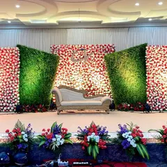 This reception stage uses a dynamic design of alternating floral and greenery panels. The angled panels create a sense of depth, while the bright red and white flowers stand out against the lush green backdrop.