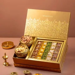 A luxury Indian sweet and dry fruit gift box for Meethi India, styled for a festive campaign. The composition uses traditional brass elements to create an opulent, celebratory feel, perfect for high-end product and packaging photography.
