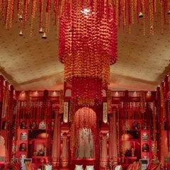 The 'Lal Bagh' mandap in Kochi, featuring a massive, handcrafted floral chandelier in shades of red and orange. This centerpiece was created by artisans from West Bengal, with each shola flower handmade, painted, and strung with mauli threads.
