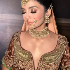 A close-up of this gorgeous bridal makeup. The focus is on the warm, bronze-toned eyeshadow, flawless skin, and traditional gold jewelry, creating a look of timeless beauty.