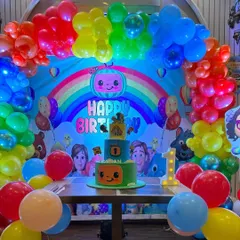 A closer look at the Cocomelon birthday cake table, framed by a colorful rainbow balloon arch and a themed backdrop.