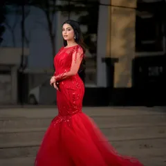 A full-length shot of a model in a red mermaid-style gown, taken outdoors for a dramatic effect.