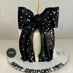 A chic and simple cake featuring a large, dramatic black fondant bow sprinkled with sugar pearls.