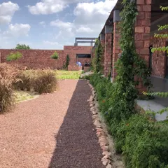 A gravel pathway runs alongside a building clad in local brick, with climbing plants beginning their journey up the pillars. This design choice ensures the architecture and landscape merge into a single, cohesive experience.