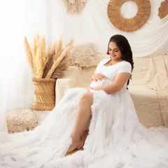 A sweet, candid moment of the mother looking down at her bump. The soft, natural light from the window adds to the ethereal feel of the scene.