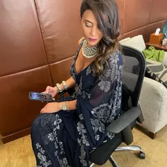 A full view of a sophisticated party look. The side-swept hair and glamorous makeup were designed to complement her elegant navy blue and silver saree.