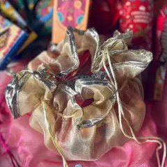 A traditional organza potli with gota work, used to hold small treats or gifts within a larger festive hamper.
